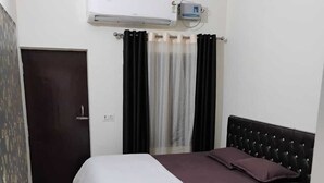A bedroom with a bed, a patterned rug, an air conditioning unit, and a door. - TabTrips Bhakti Dham Stay (Varanasi)