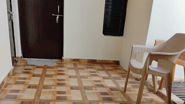 A room with a patterned wooden floor, a dark wooden door, and a plastic chair. - TabTrips Bhakti Dham Stay (Varanasi)