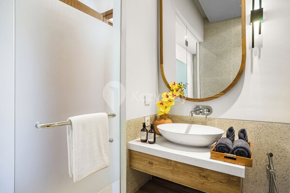 Un baño moderno con lavamanos blanco, tocador de madera y un perchero para toallas.