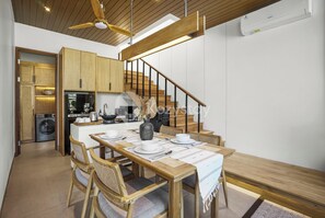 A modern kitchen with wooden cabinets, a dining area with a wooden table and chairs, and a staircase with a wooden railing.