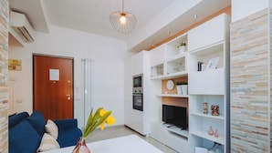 A modern living room with a white sofa, a dining table with a vase of flowers, and built-in shelving with decorative items.