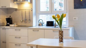 A modern kitchen with white cabinets, a stainless steel range hood, and a window with a view of buildings.