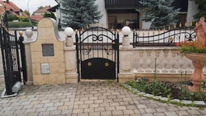 Una entrada cerrada con un portón de metal negro, un muro de piedra y una valla decorativa con adornos esféricos.