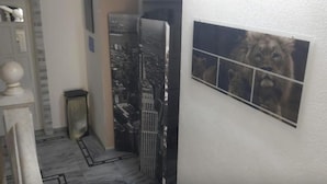 Un pasillo estrecho con un mural de paisaje urbano en la pared, una puerta decorada con un globo terráqueo y un cuadro enmarcado de un león.