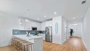 A modern kitchen with white cabinets, a stainless steel refrigerator, and wooden bar stools. - Blue Wave by Team Joseph Ellen (Jacksonville Beach)
