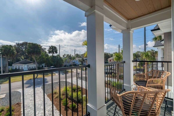 A balcony with wicker furniture, a clear view of the street, and a white building in the background.