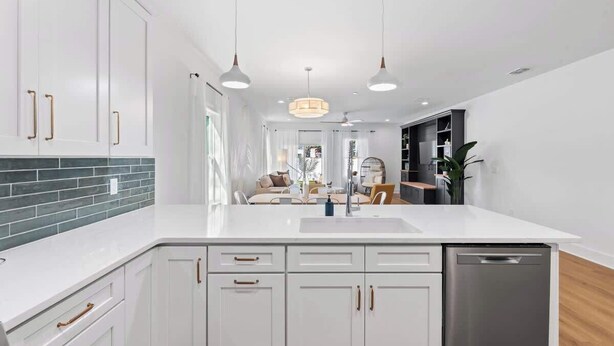 Une cuisine moderne avec des meubles blancs, un îlot central, des luminaires suspendus et une vue sur l’espace de vie.