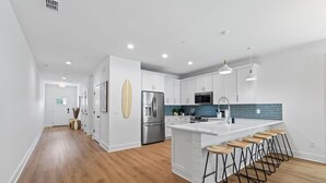 Une cuisine moderne avec des meubles blancs, un réfrigérateur en acier inoxydable, un four à micro-ondes et un grand îlot central doté de tabourets de bar.