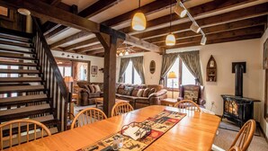 A cozy interior with a wooden staircase, a dining table with a patterned runner, and a black wood-burning stove. - A Wonderful Vacation Home Set in the Woods with Unique Envelope Architecture (Bessemer)