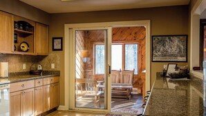 A kitchen with wooden cabinets, a granite countertop, and a sliding glass door leading to a dining area with a view of the mountains. - A Wonderful Vacation Home Set in the Woods with Unique Envelope Architecture (Bessemer)