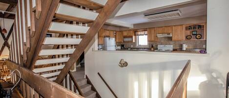A staircase with wooden railings leading to a kitchen area with wooden cabinets and a white countertop.