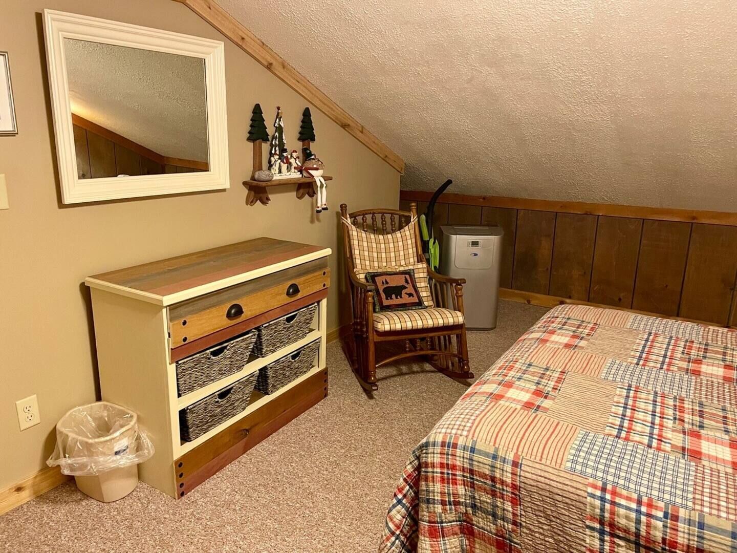 A bedroom with a bed, a dresser, a chair, a mirror, and a small refrigerator.