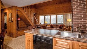 A cozy cabin-style kitchen with wooden walls, a built-in stove, granite countertops, and a dishwasher.
