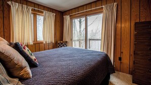 A bedroom with a large bed, wooden walls, and a view through the windows.