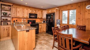 A kitchen with wooden cabinets, a granite countertop, a stove, a refrigerator, and a dining table with chairs.