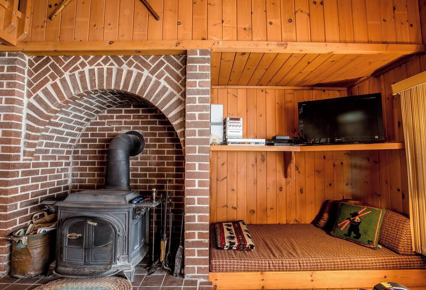 A cozy cabin with a brick fireplace, a television on a shelf, and a comfortable seating area with a blanket.