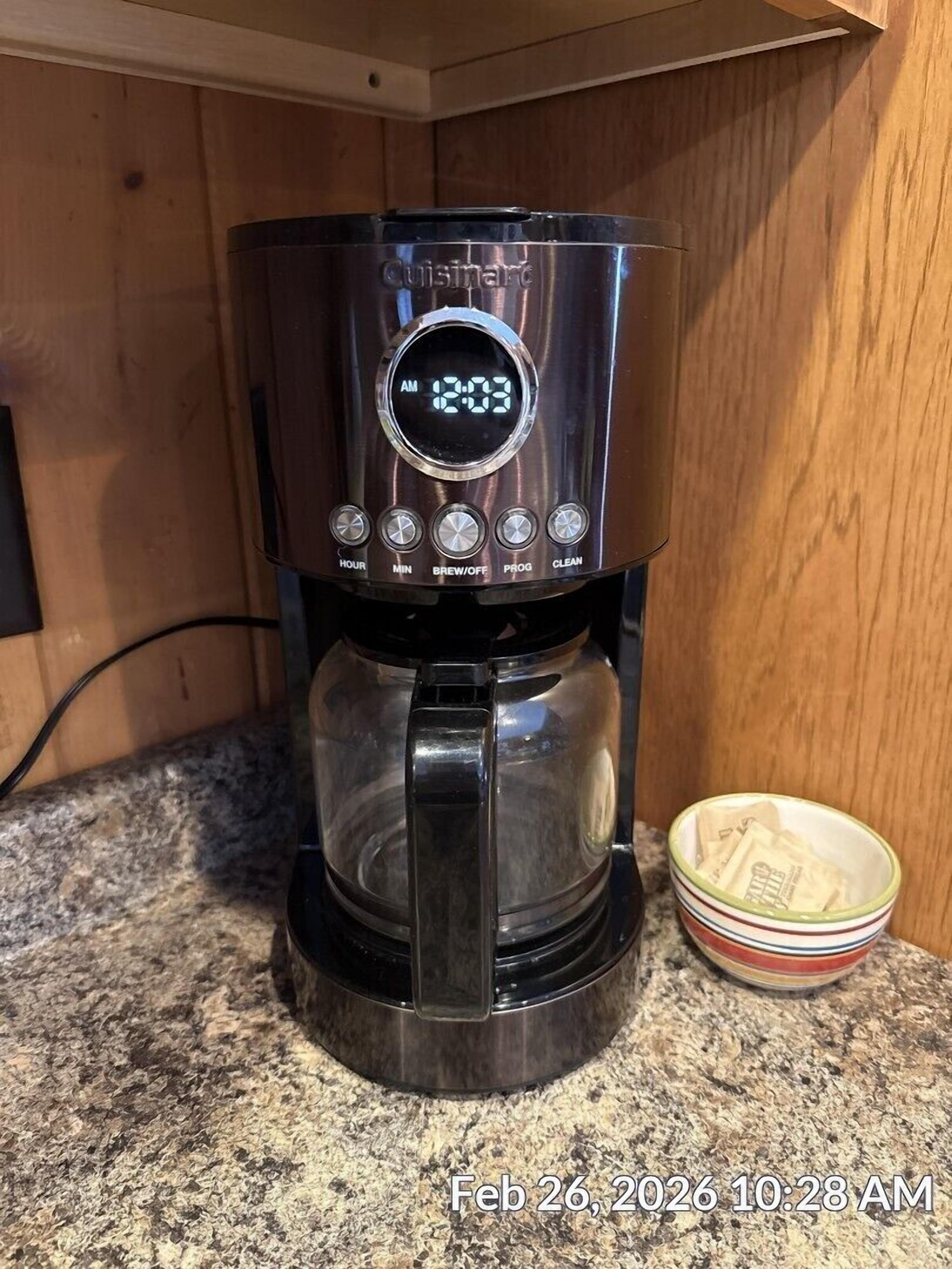 A black Cuisinart coffee maker with a digital clock displaying 12:03 AM, a timer, brew-off, and clean buttons, placed on a granite countertop next to a bowl with tea bags.