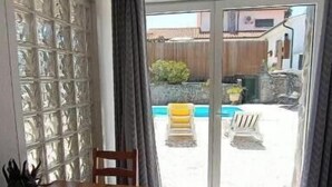 A room with a wooden table and chairs, a glass block wall, and a sliding glass door leading to an outdoor area with a pool and furniture. - Casa Machuca with swimming pool (Tomar)