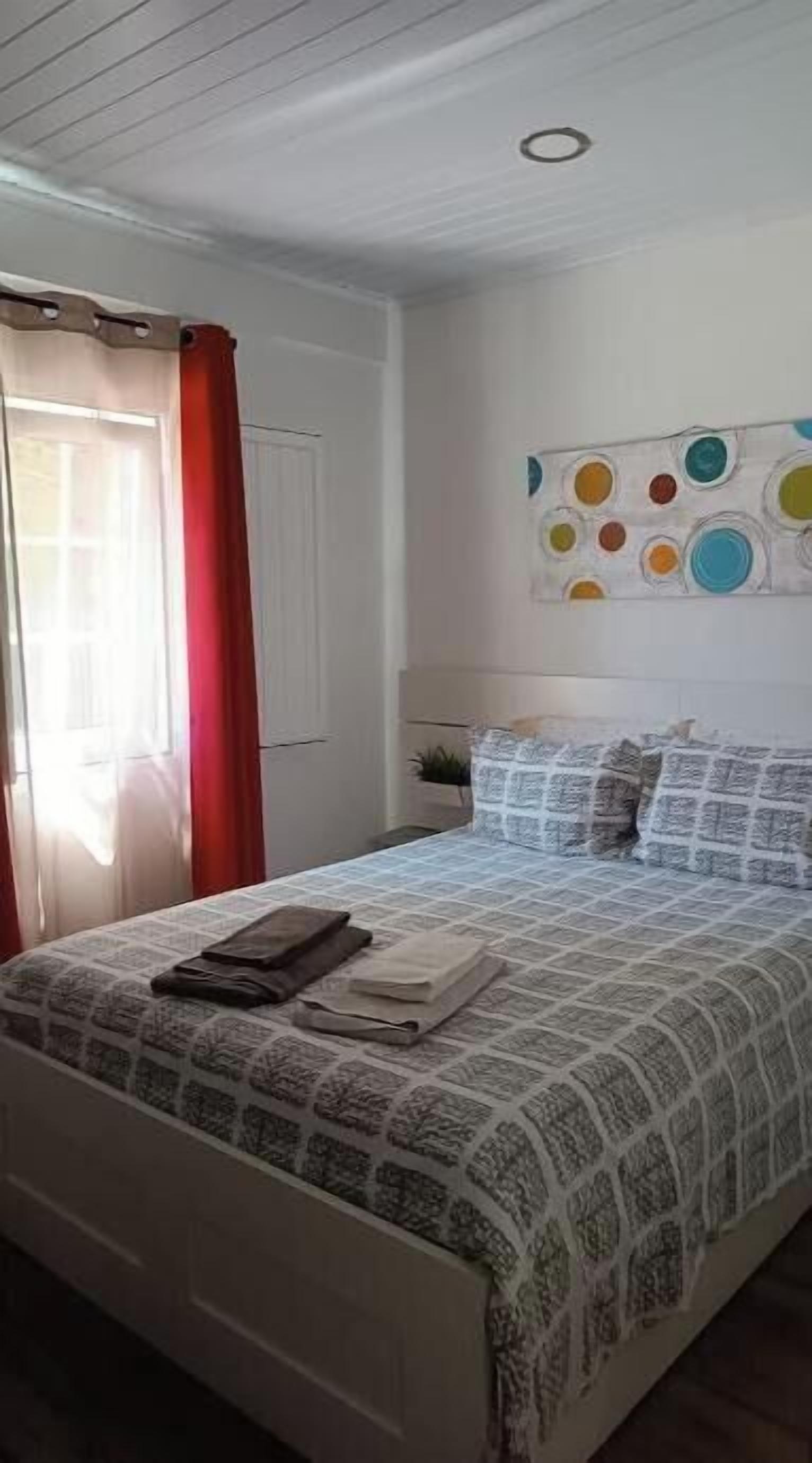 Une chambre à coucher avec un lit, une fenêtre ornée de rideaux rouges et un mur décoré d’un motif circulaire aux couleurs vives.