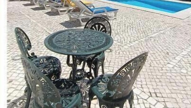 A pool area with a tiled patio, a table with chairs, and a large tree. - Casa Machuca with swimming pool (Tomar)