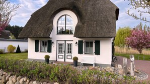 A traditional thatched-roof house with a white facade, a central arched window, and green shutters. - Vacation home Schilfrohrsänger 21 - Close to nature (Fuhlendorf)