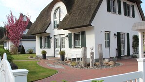 A white house with a thatched roof, green shutters, and a white bench in the front yard. - Vacation home Schilfrohrsänger 21 - Close to nature (Fuhlendorf)