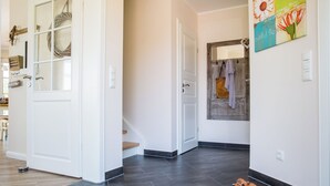 A hallway with a wooden floor, a white door, and a wall-mounted artwork. - Vacation home Schilfrohrsänger 21 - Close to nature (Fuhlendorf)