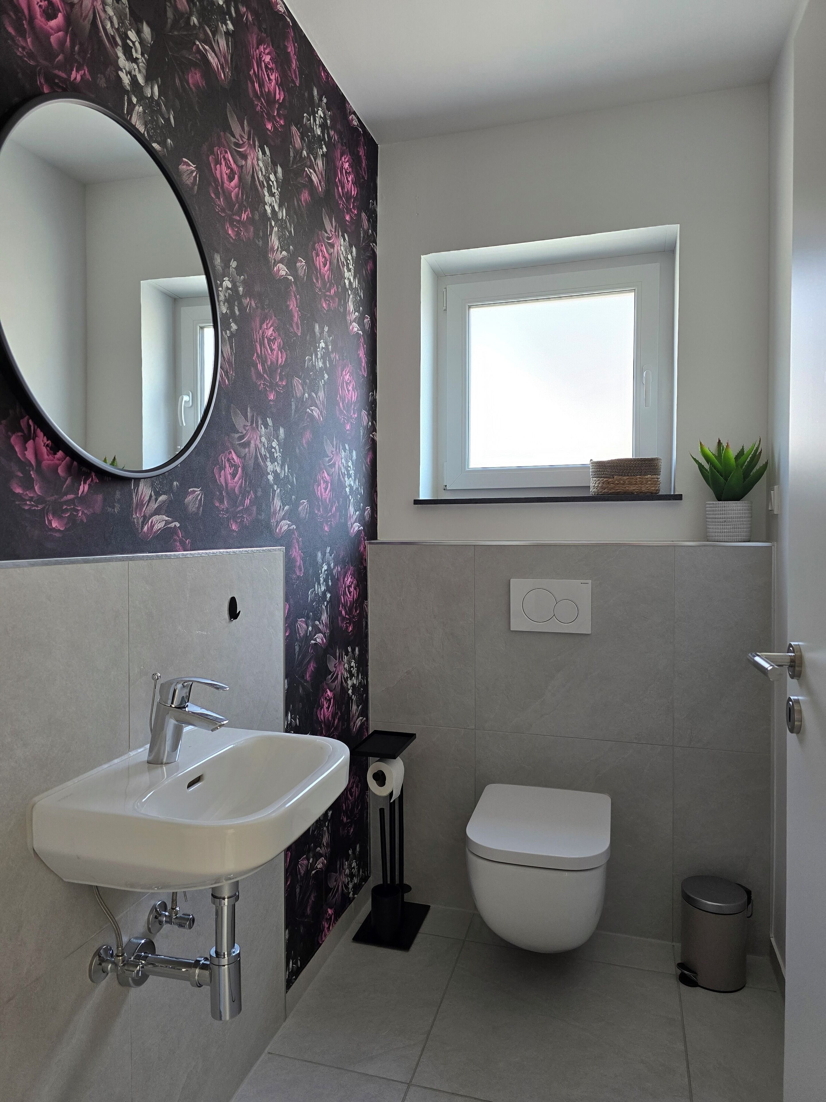 A modern bathroom with a white sink, a toilet, and a window above the toilet.
