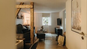 Un accogliente soggiorno con travi in legno a vista, un divano, un tavolino, una TV e una finestra con vista sul verde.