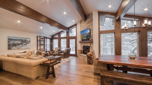 A spacious living room with a wooden ceiling, large windows, a fireplace, and a dining area.