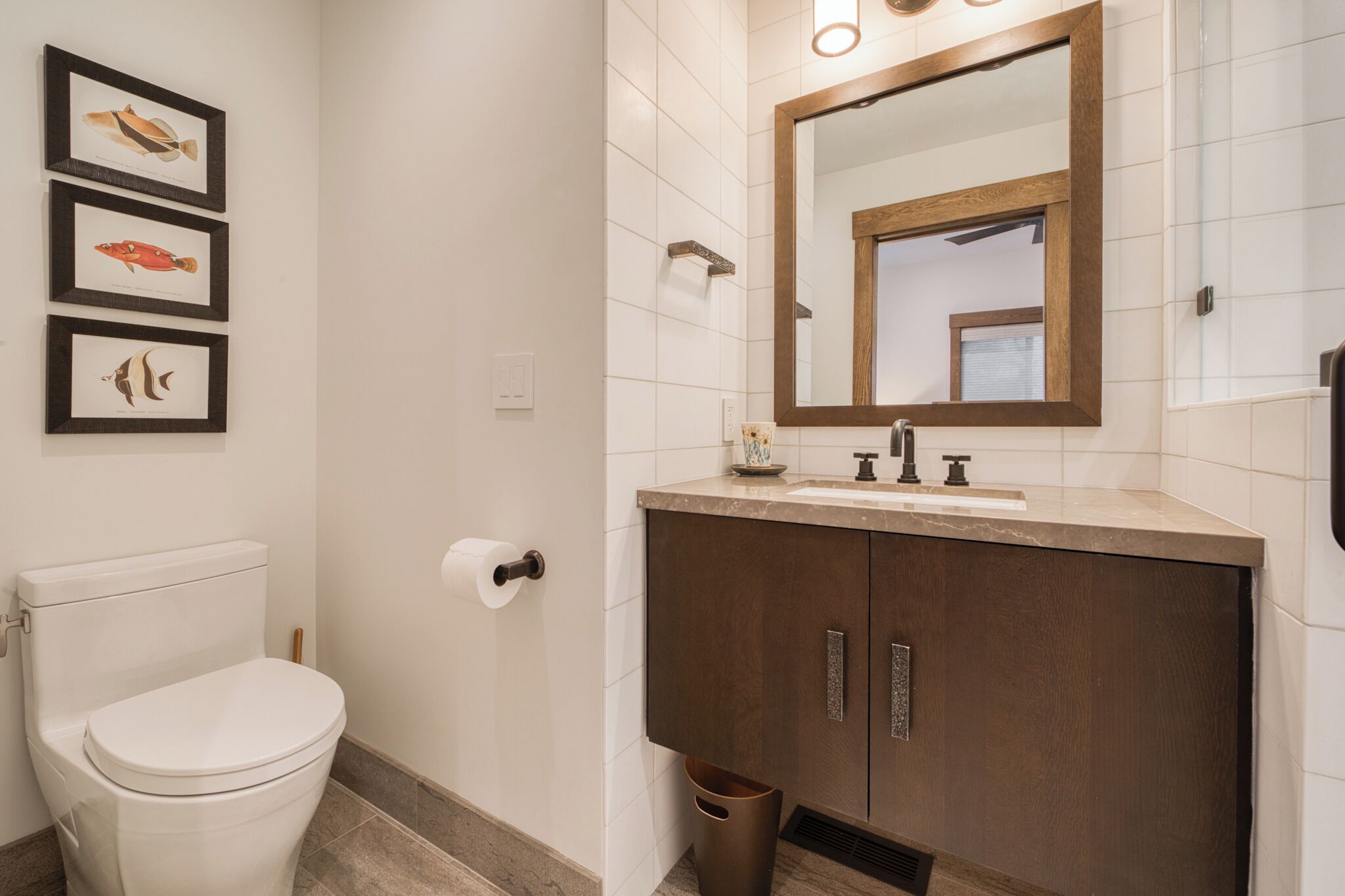 Een badkamer met toilet, wastafel, badkamermeubel, spiegel en wanddecoraties van ingekaderde visillustraties.