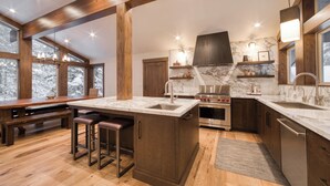 A modern kitchen with wooden beams, a large island with stools, a built-in oven, and a marble backsplash.