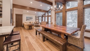 A spacious dining area with a wooden table and benches, large windows with a snowy view, and a cozy seating area with a sofa and chairs.