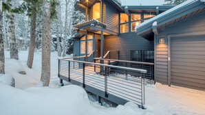 A modern house with a covered deck, surrounded by snow-covered trees.