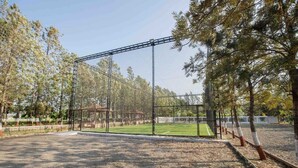 Un terrain de sport clôturé, doté d’une zone protégée par un filet, entouré d’arbres et offrant une vue sur un ciel dégagé.