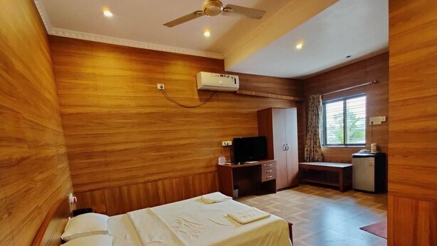 Une chambre d’hôtel avec un mur en bois, un lit, un bureau, une télévision et une fenêtre.