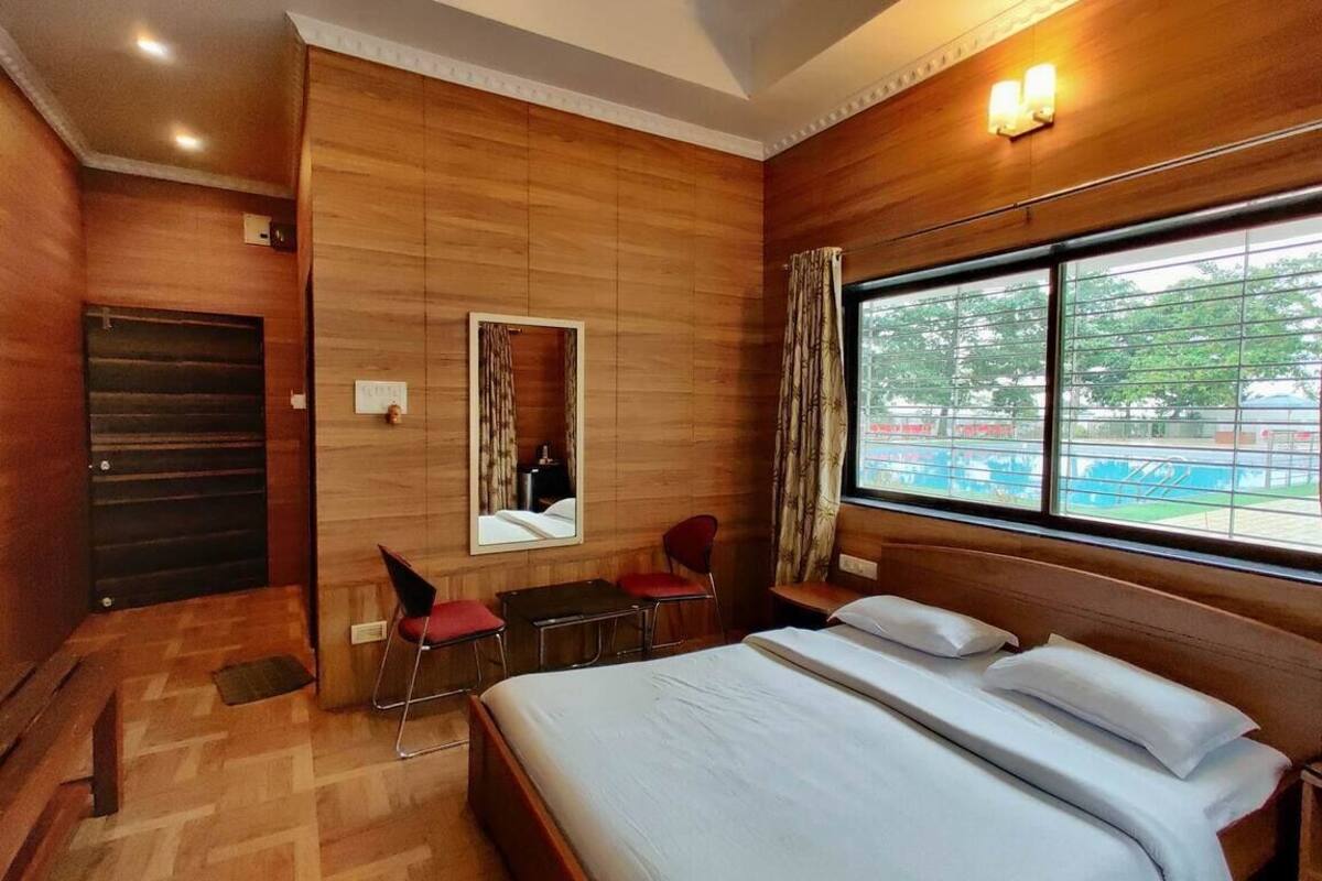 A hotel room with a wooden wall, a large bed, a desk, a chair, and a window with a view of the outside.