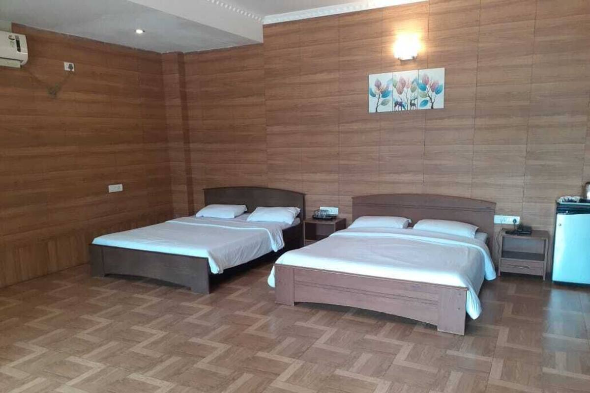 A hotel room with two beds, wooden walls, a painting, and a small desk with a lamp.