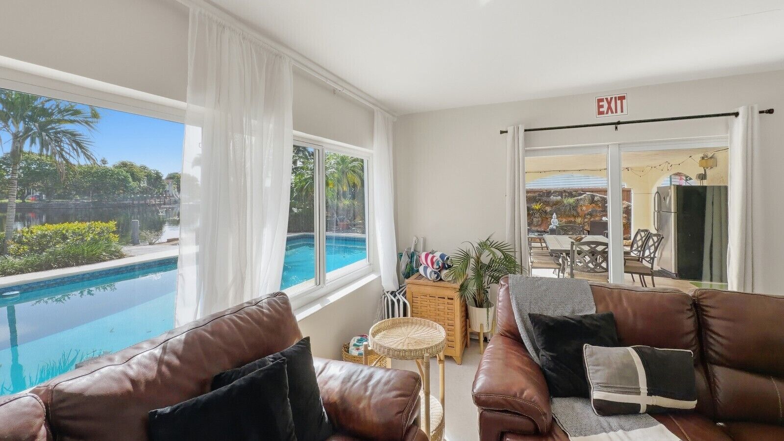 Una habitación con vista a la piscina, un sofá de cuero marrón, una mesita de mimbre y una señal de salida.