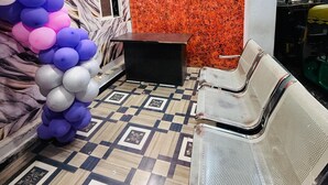 Zona de recepción con pared de mármol, piso estampado, mostrador de recepción y fila de sillas.