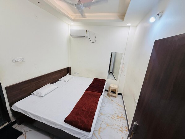 Habitación de hotel con cama, ventilador de techo, aire acondicionado, un taburete pequeño y una puerta.