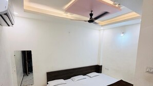 Un dormitorio con cama, ventilador de techo, un taburete pequeño y un espejo.