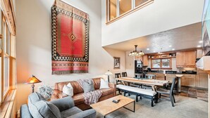 A spacious living area with a sofa, coffee table, and dining table. A kitchen is visible in the background with wooden cabinets and a window. - Park City in Prime Location/Sleeps 7/Summer AC (Park City)