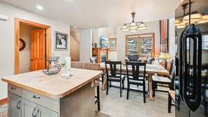 A modern kitchen with a central island, wooden cabinets, and a dining area with chairs and a table. - Park City in Prime Location/Sleeps 7/Summer AC (Park City)