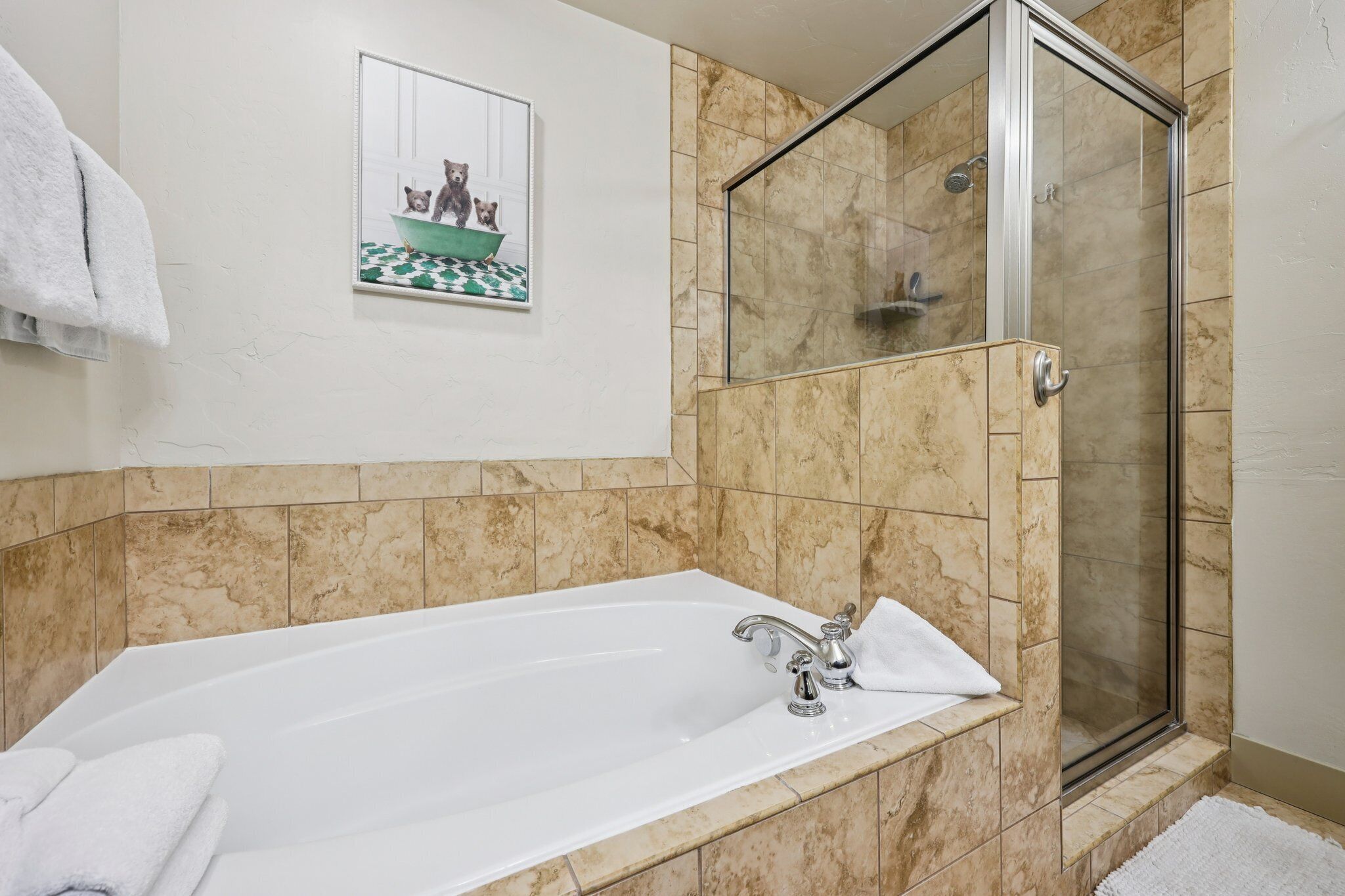 Un baño con bañera, cabina de ducha con mampara de vidrio y un cuadro en la pared.