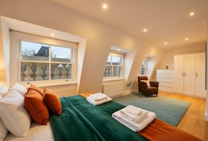 Een slaapkamer met een bed, kussens, een stoel, een radiator en een garderobe.