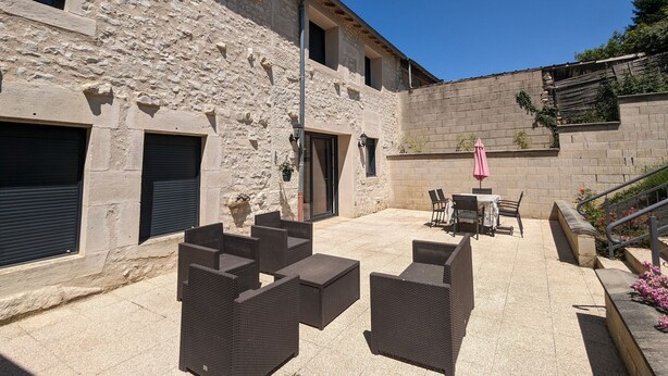 An outdoor patio with wicker furniture, a stone building, and a pink umbrella.