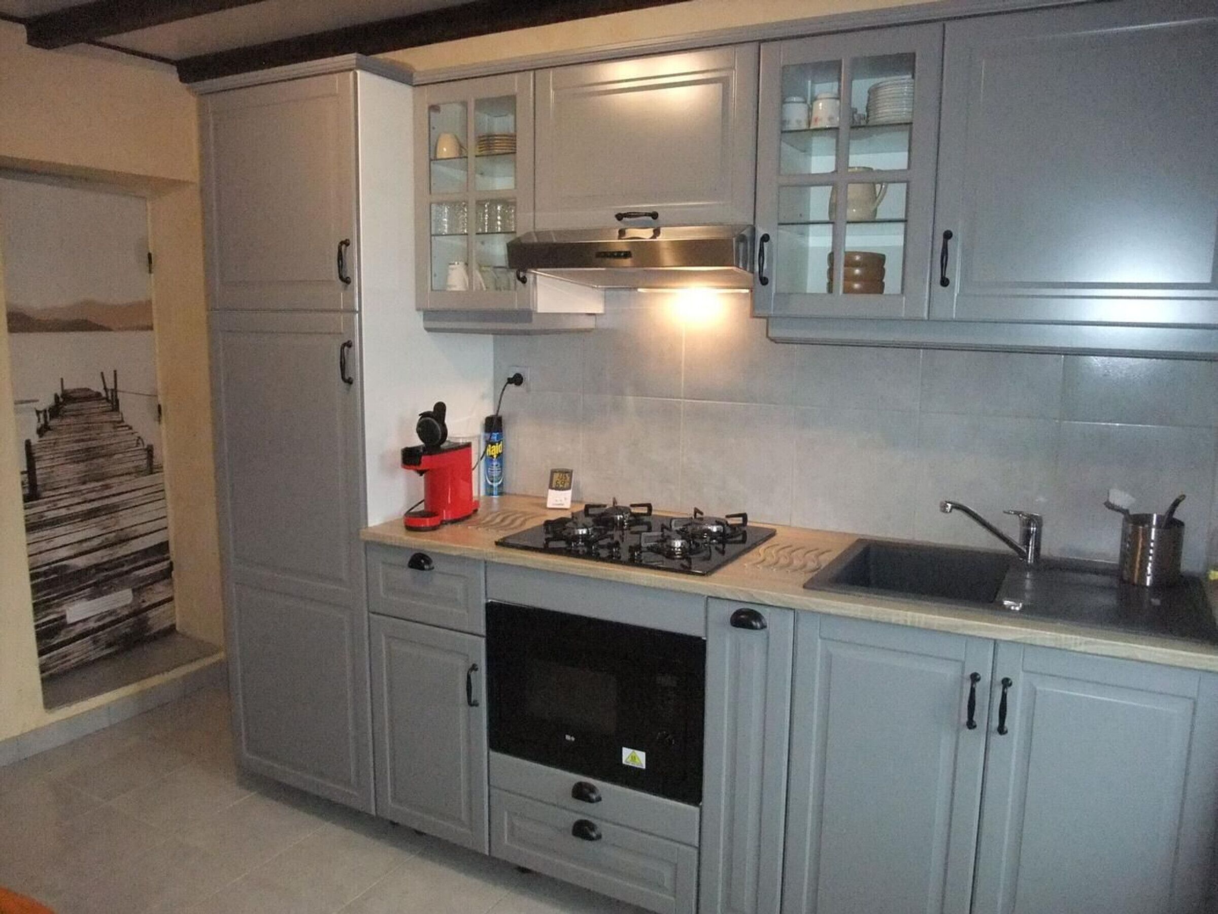 Une cuisine moderne avec des meubles gris, une hotte en acier inoxydable, une cuisinière à gaz et un four encastré.