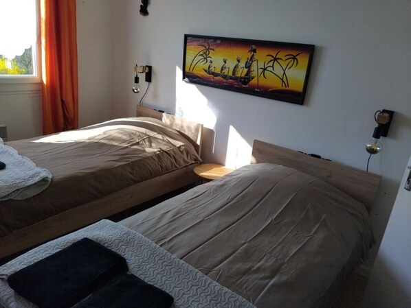A room with two beds, a painting on the wall, and a window with curtains.