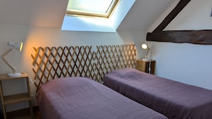 Un dormitorio con dos camas, cabecero de madera, tragaluz y mesita de noche con lámpara.